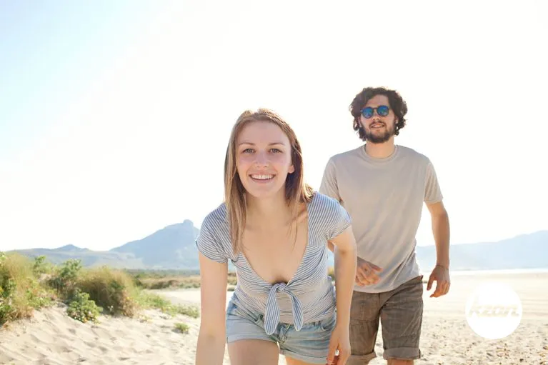 Attractive couple walking together on a sunny white sand beach on a summer holiday destination with blue sky and sunshine, outdoors. Travel lifestyle with man and woman being playful, coastal exterior.