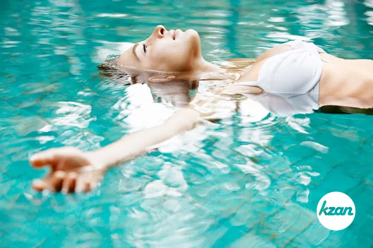 Attractive young woman floating in a swimming pool with her arms outstretched, looking at the sky.
