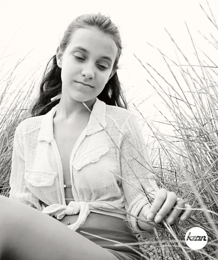 Black and white portrait of beautiful teenager girl thoughtful on beach sand dunes touching long grass, relaxing and enjoying summer holiday vacation, outdoors. Adolescent recreation lifestyle.