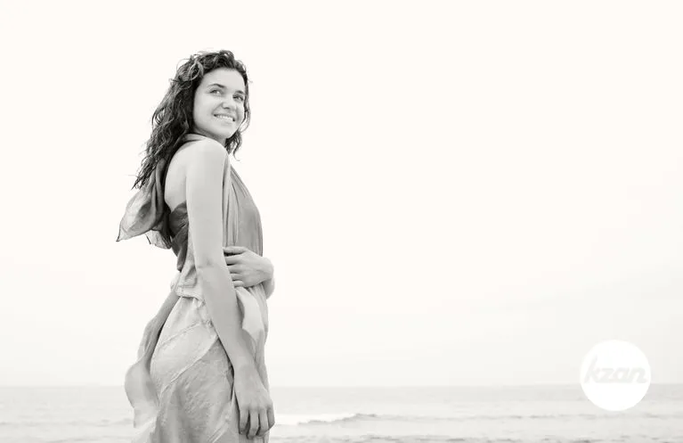 Black and white view of a serene beautiful young woman on a beach with a silk sarong fabric wrapped around her body, turning and smiling. Well being healthy lifestyle, body figure.