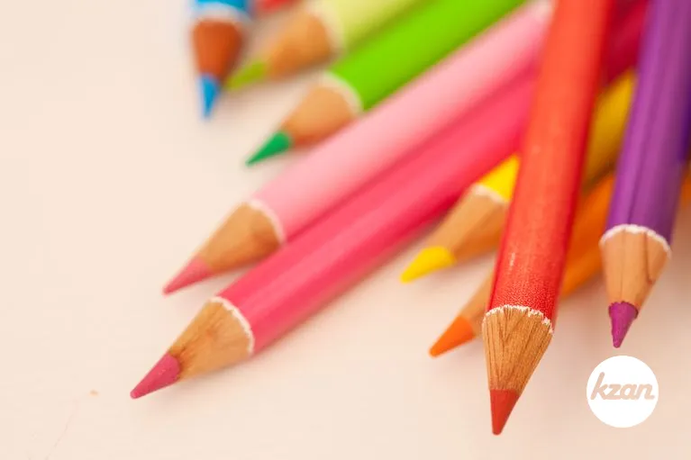 Bunch of multiple colored drawing pencils on a school desk, interior.