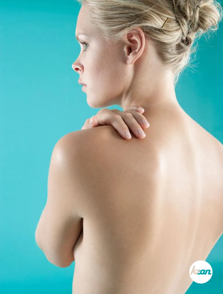 Close up view of a woman's bare back with her hand on her shoulder.