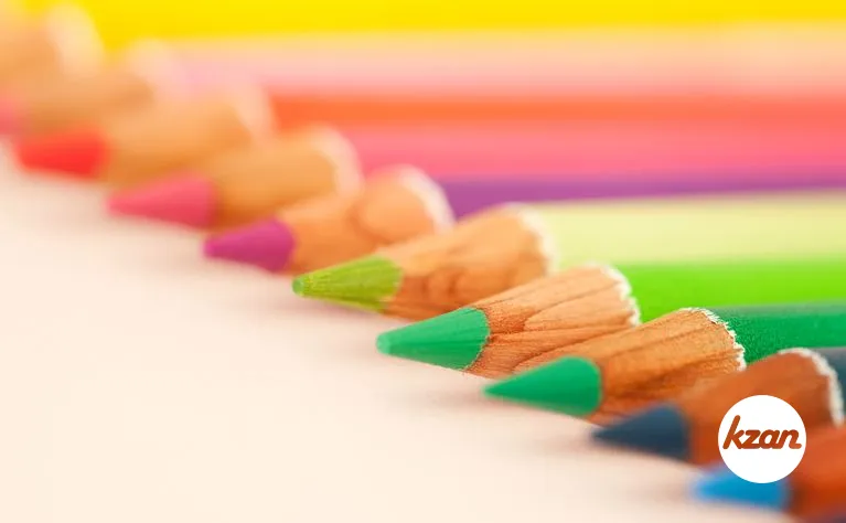 Diagonal line of multi colored drawing pencils on a white writing desk, over head close up detail view.