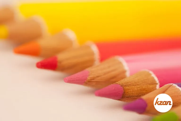 Diagonal perspective of various multi colored drawing pencils on a white writing desk, over head close up detail view.