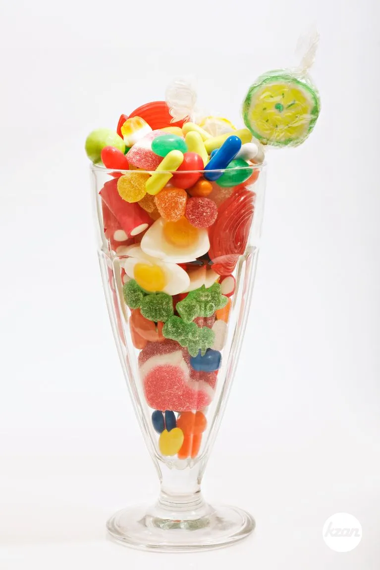 Full view of a transparent glass full of an assortment of different colorful candy and sweets isolated against a white background. Children party feel.