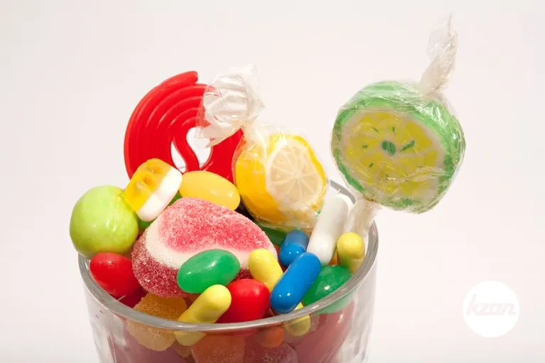 Still life of a glass container with different colorful candy sweets, fruity sticks, liquorice and jelly beans isolated against a white background. Indulgence and naughty sugar and fat full food temptation.