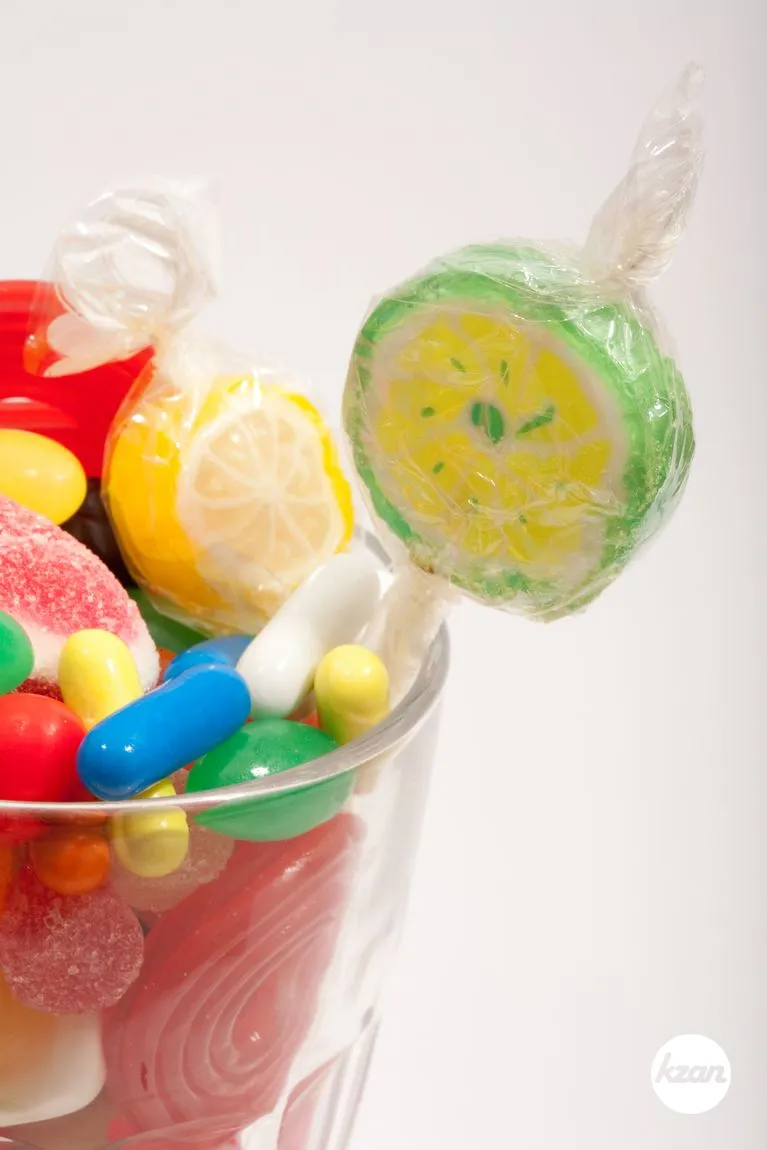 Still life of a glass container with different colorful candy sweets, fruity sticks, liquorice and jelly beans isolated against a white background. Indulgence and naughty sugar and fat full food temptation.