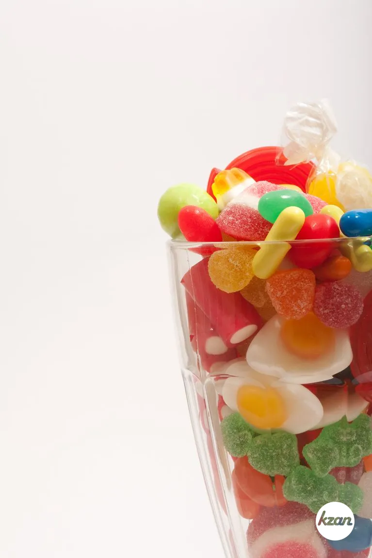 Still life of a glass container with different colorful candy sweets, liquorice and jelly beans isolated against a white background. Indulgence and naughty sugar and fat full food temptation, interior.