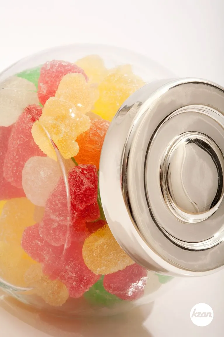 Still life of a glass jar container with different colorful candy sweets and jelly beans isolated against a white background. Indulgence and naughty sugar and fat full food temptation.