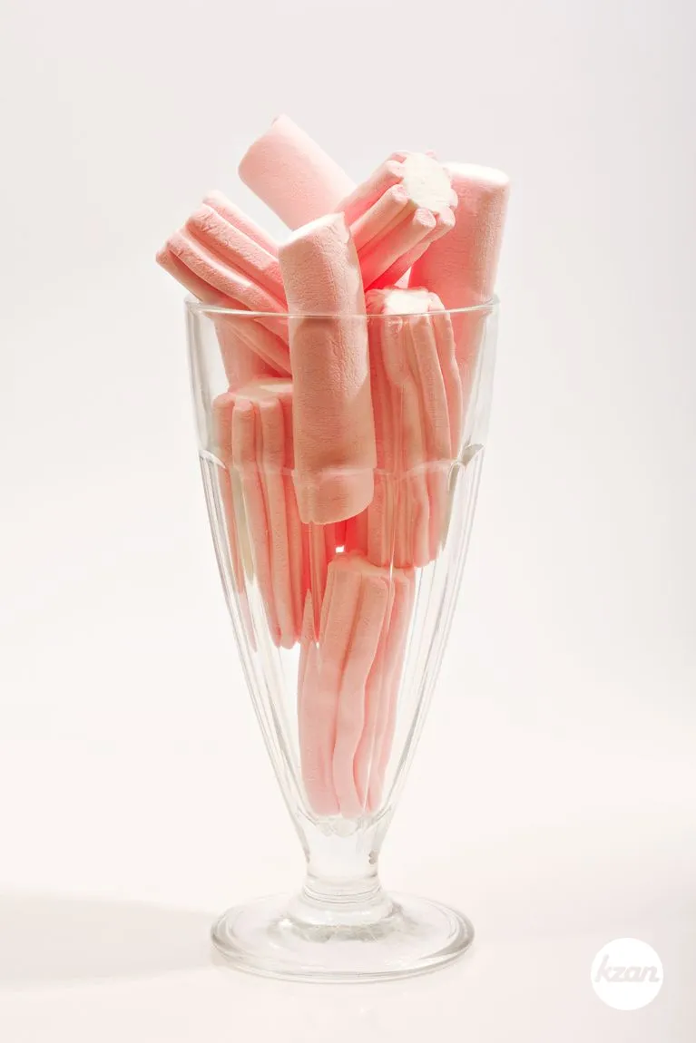 Still life view of a glass full of sweet pink marshmallows isolated against a white background, interior. Tempting and tasty party indulgence candy eating and naughty food eating.